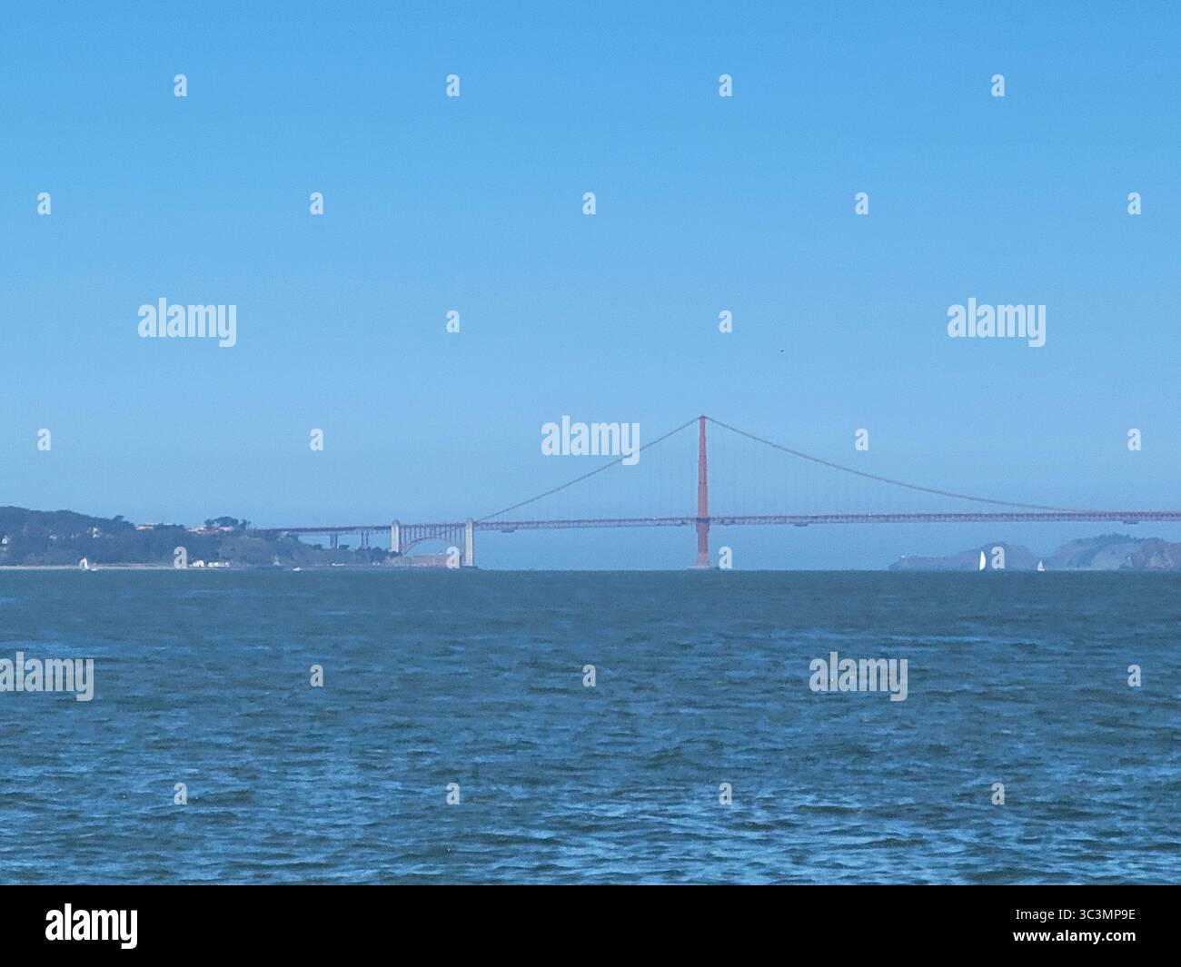 A view of Golden Gate Bridge, San Francisco as seen from Alcatraz Island. A sailboat  glides under the bridge on this cloudless, clear day. - Smartphone Captured Stock Image