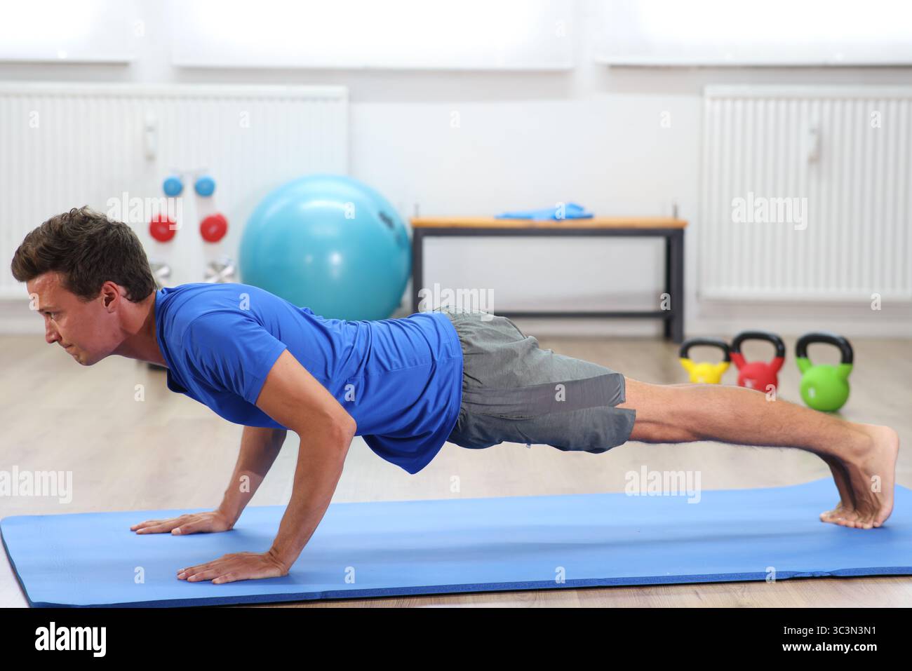 young man, blue shirt on fitness mat doing push-ups Stock Photo