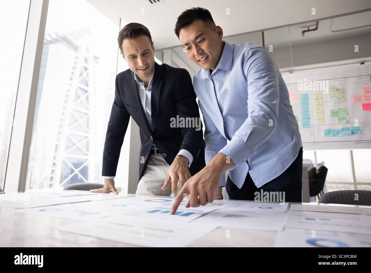 Two diverse teammates analyzing printed graphs and charts Stock Photo