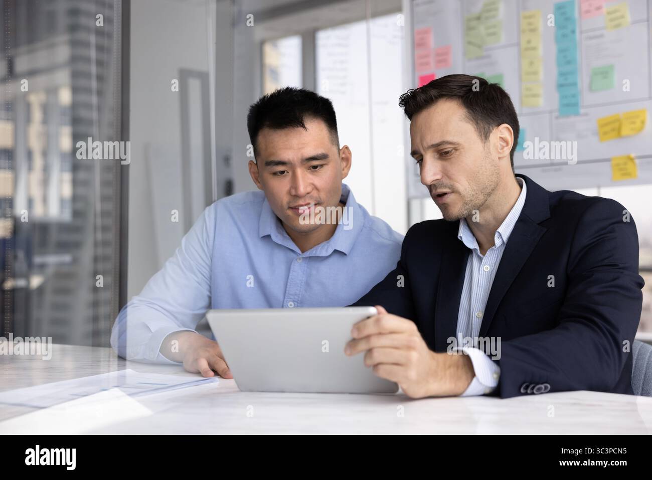 Two professional men looking at tablet screen seated at table Stock Photo
