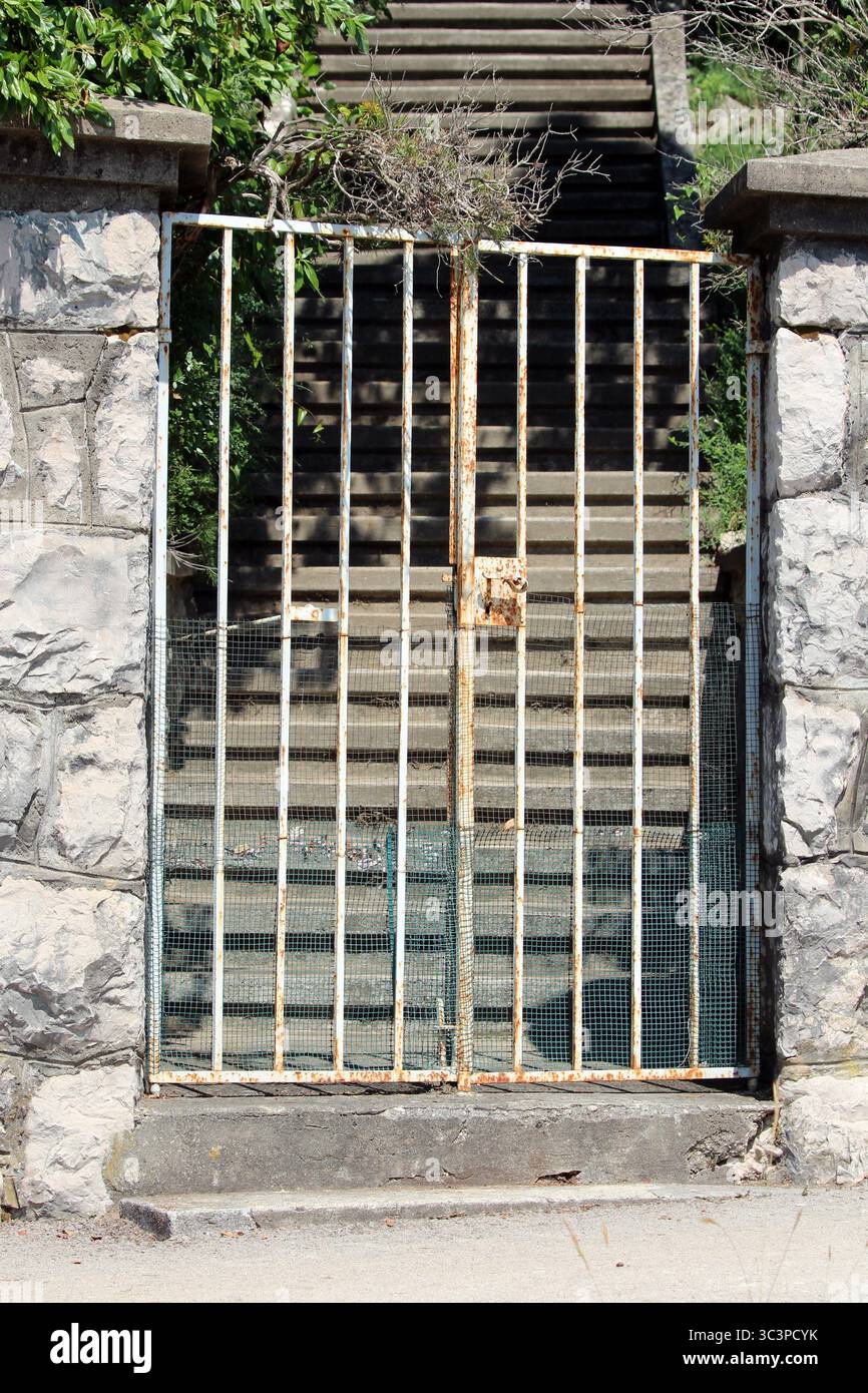 A tall, vertical-barred iron gate with areas of rust and mesh wire at ...