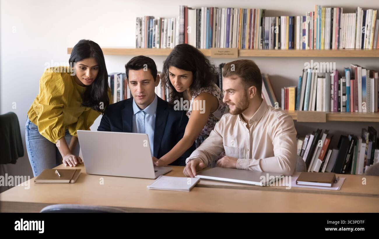 Multiethnic professionals gathered around laptop, collaborating on project or presentation Stock Photo