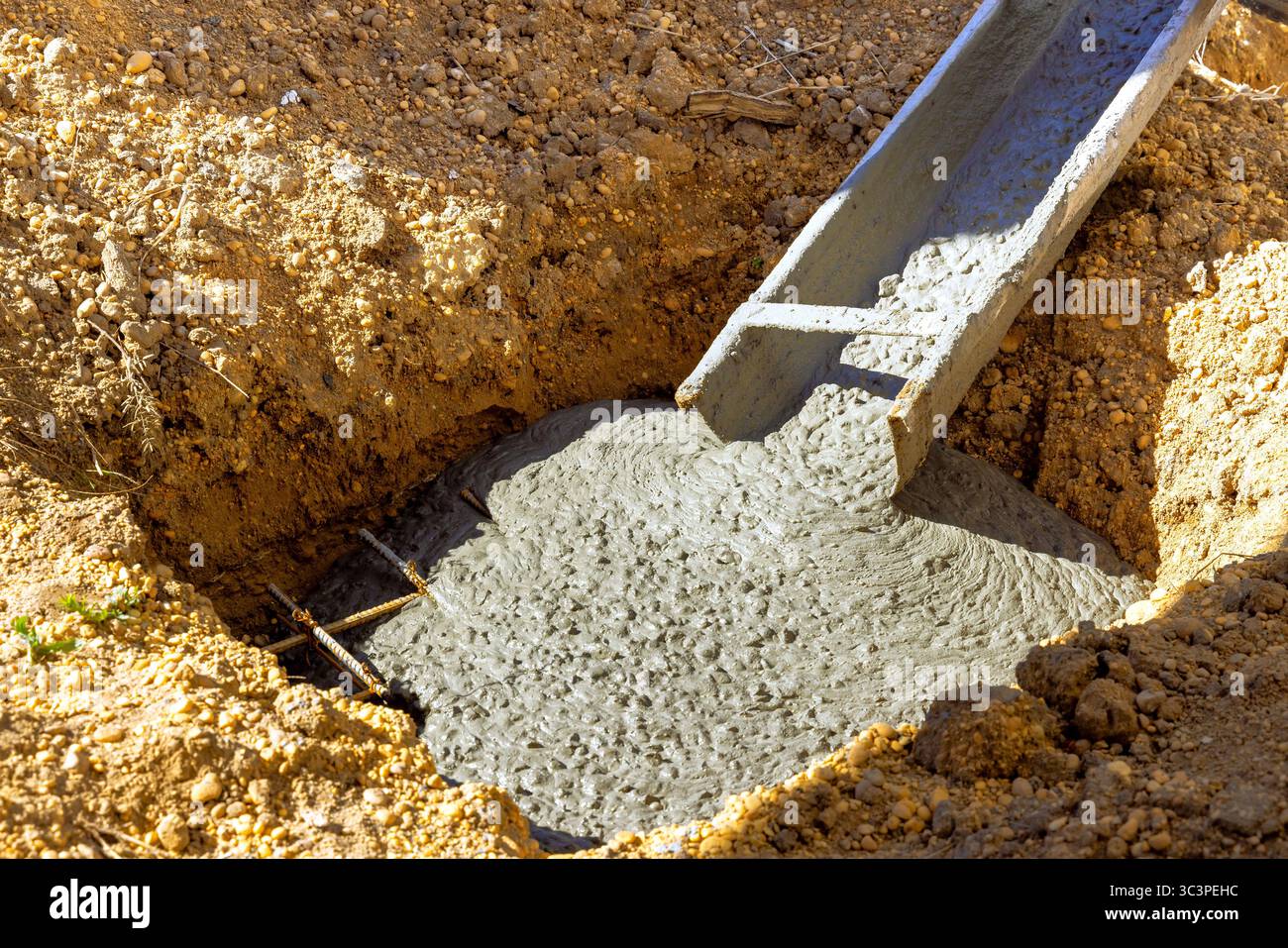 Workers pour fresh concrete into trench at construction site, ensuring solid foundations for new structure. Stock Photo