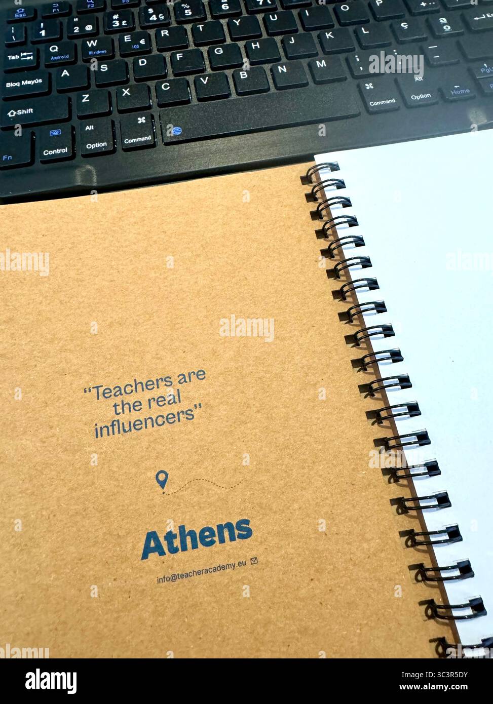 Close-up of a spiral-bound notebook with the quote 'Teachers are the real influencers' printed on the cover, placed next to a computer keyboard. - Smartphone Captured Stock Image