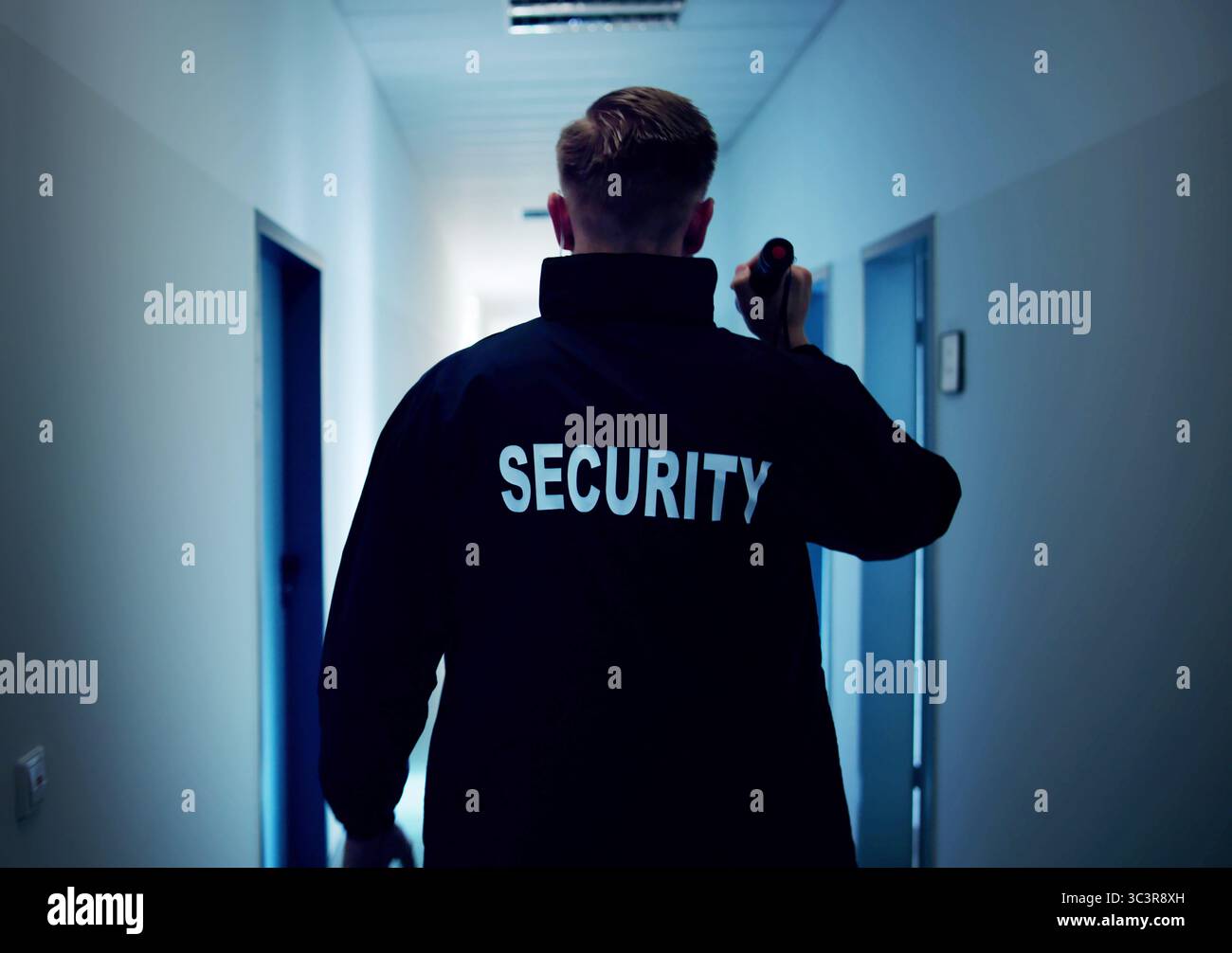 Night Security Guard Patrolling Warehouse In Uniform With Flashlight, Ensuring Safety. Stock Photo