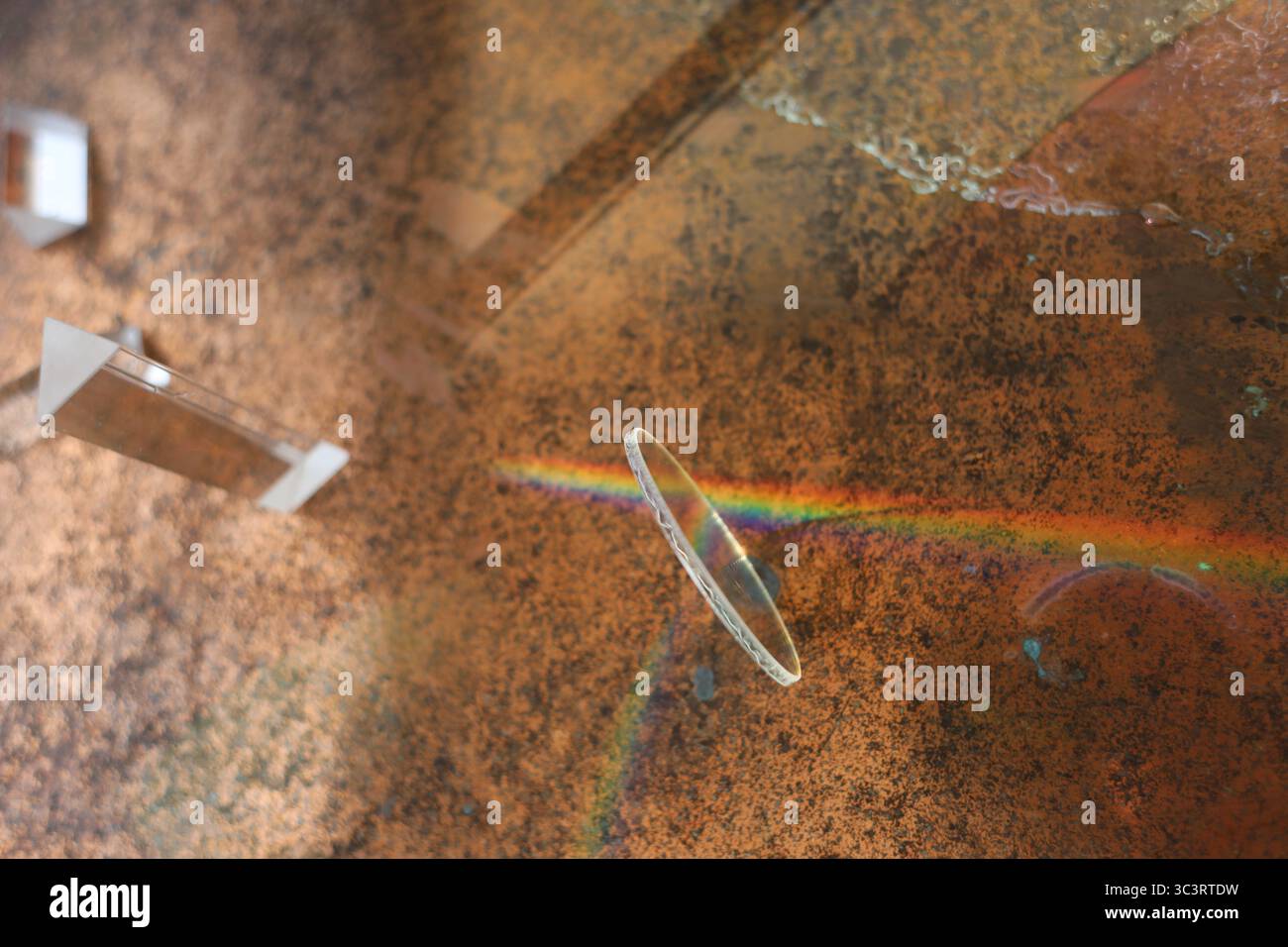 Rainbow is reflected in a broken piece of glass on a brown surface Stock Photo
