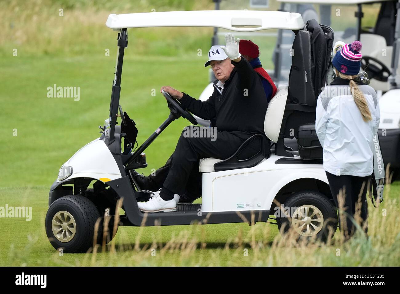 President Donald Trump waves to reporters as he steers his golf cart at ...