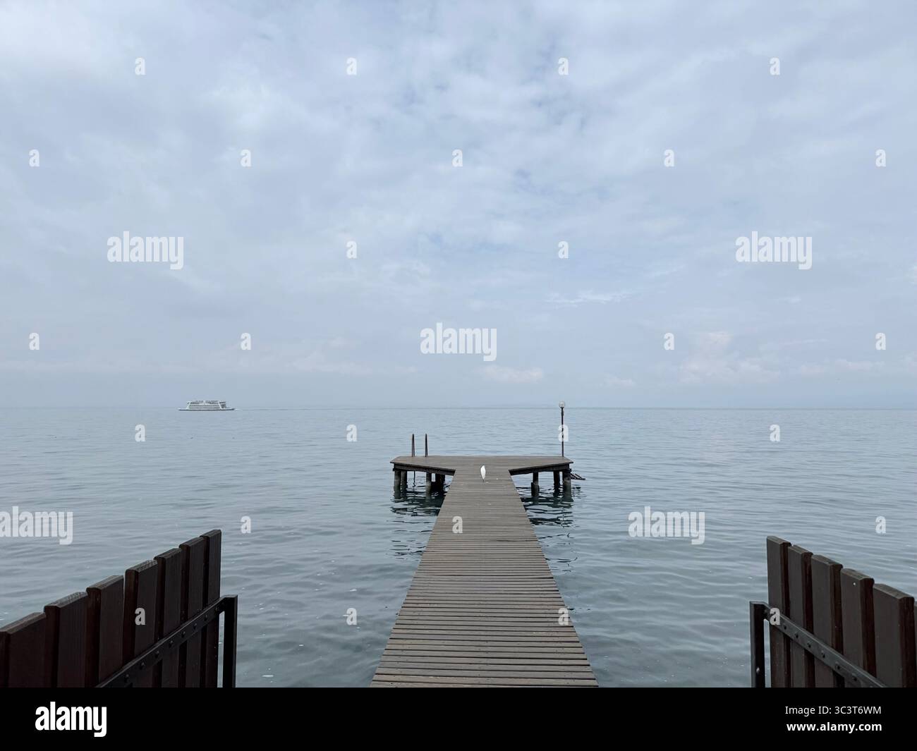 Bird on jetty early in the morning with ferry in distance at Lazise on Lake Garda, Italy - Smartphone Captured Stock Image