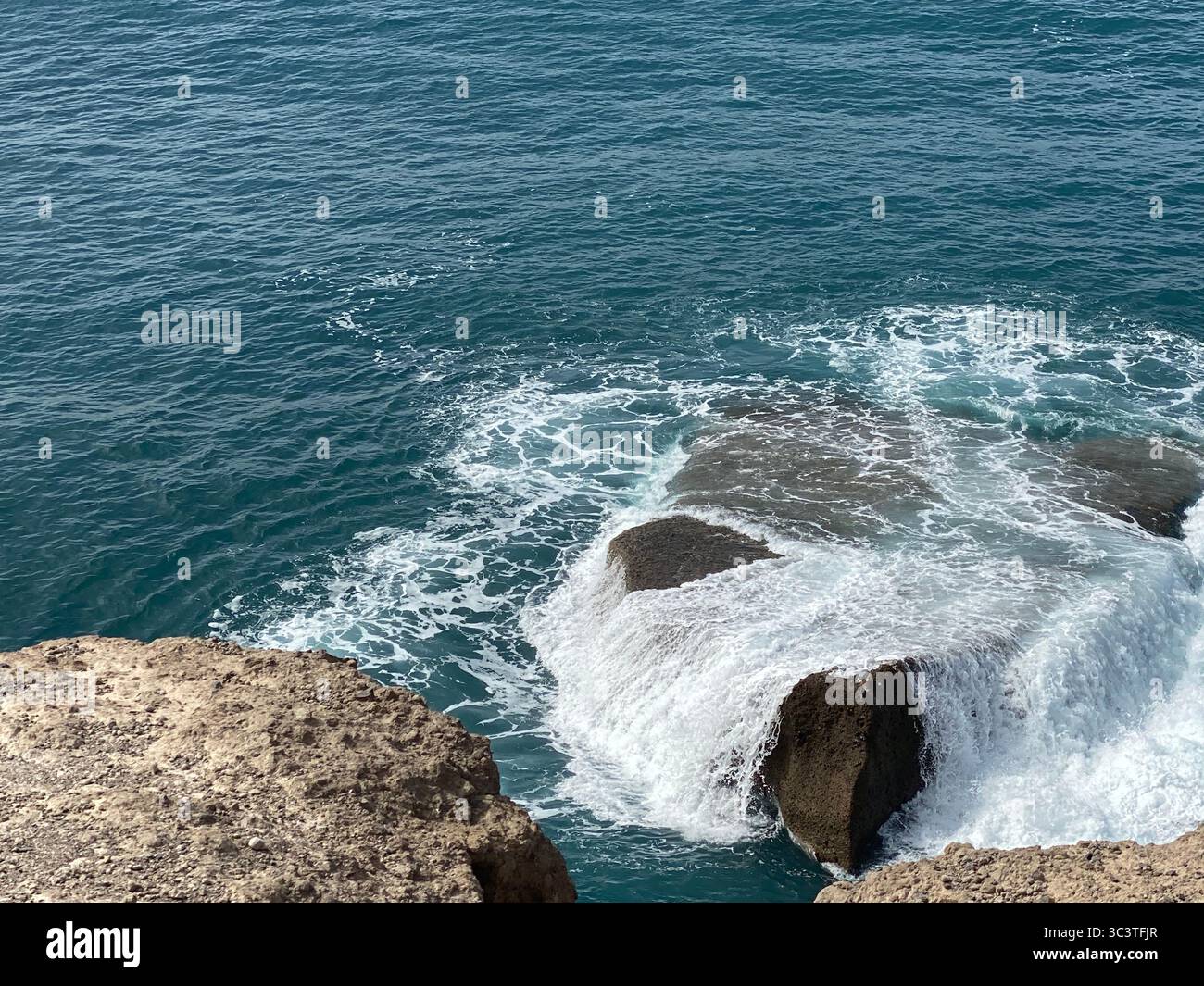 Waves crashing against the rocky shore under a clear, blue sky in Canary Islands - Smartphone Captured Stock Image