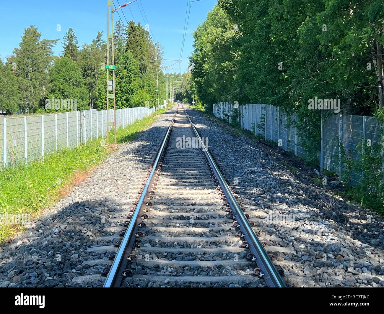 Train tracks extend through a lush green landscape under a bright blue sky. - Smartphone Captured Stock Image