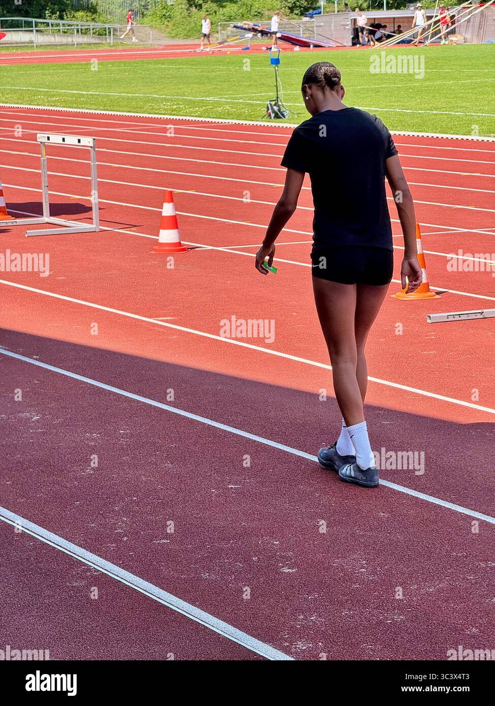 Athlete walking on a red running track near hurdles and orange cones at a sports stadium in Lübeck, Germany. - Smartphone Captured Stock Image