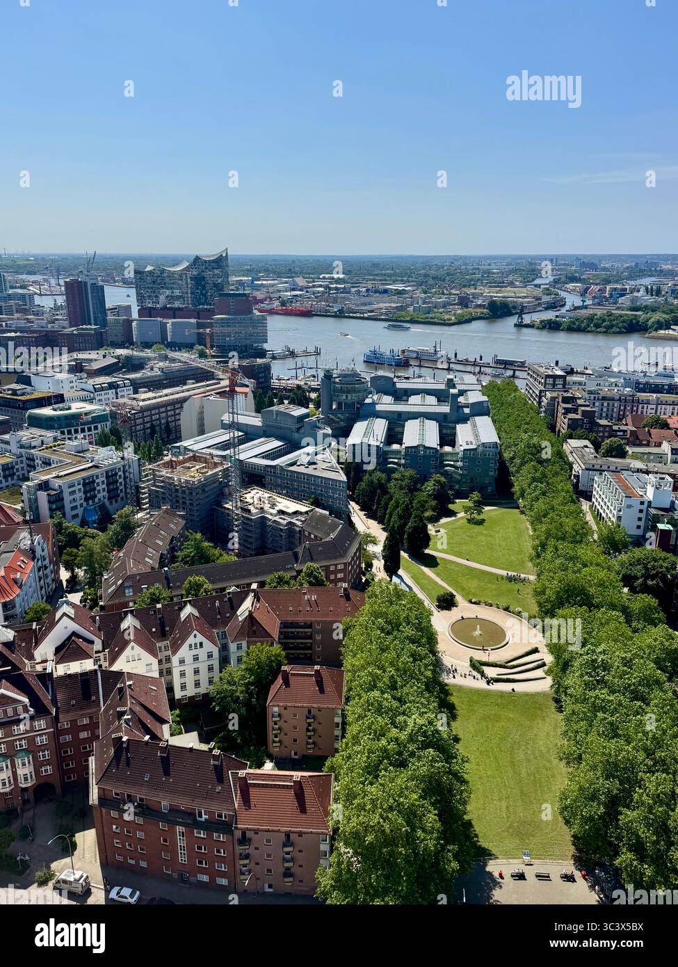 Aerial view of Hamburg cityscape from the top of St. Michael's Church, showcasing the Elbe River, urban buildings, and green parks on a clear sunny da - Smartphone Captured Stock Image