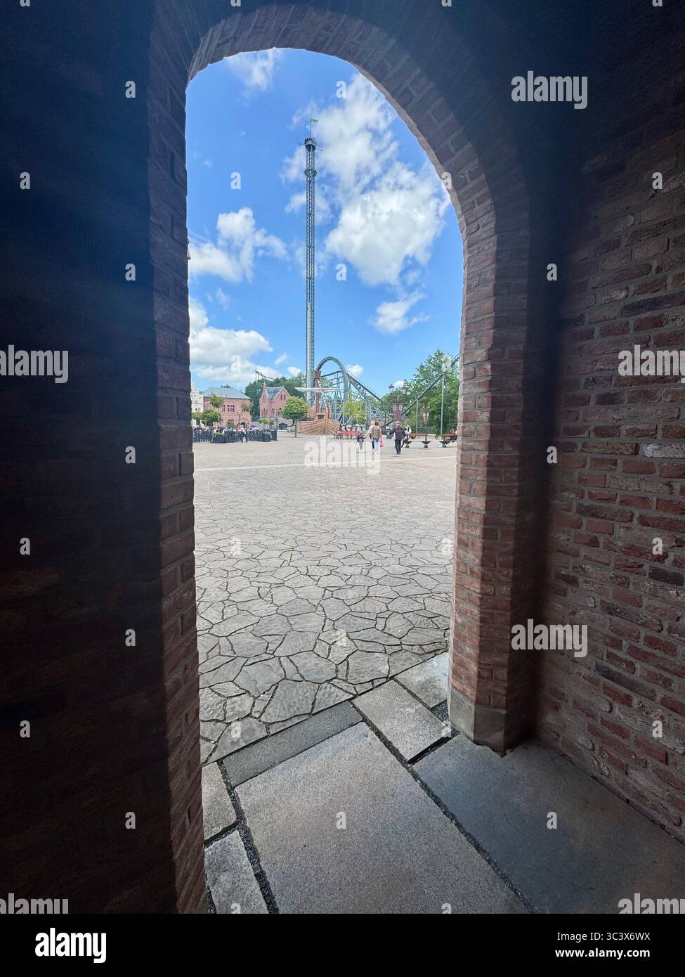 Scenic view of amusement rides at Hansa Park, Germany, seen through a brick archway. The photograph captures the vertical drop tower and roller coaste - Smartphone Captured Stock Image