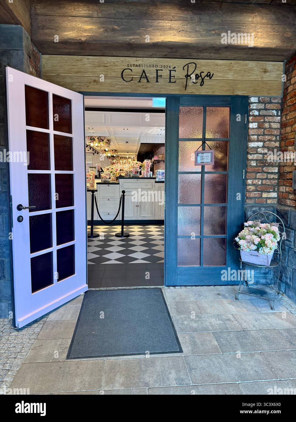 Entrance of Café Rosa at Hansa Park in Sierksdorf, Germany, featuring a charming rustic style with pastel doors and floral decoration, inviting guests - Smartphone Captured Stock Image