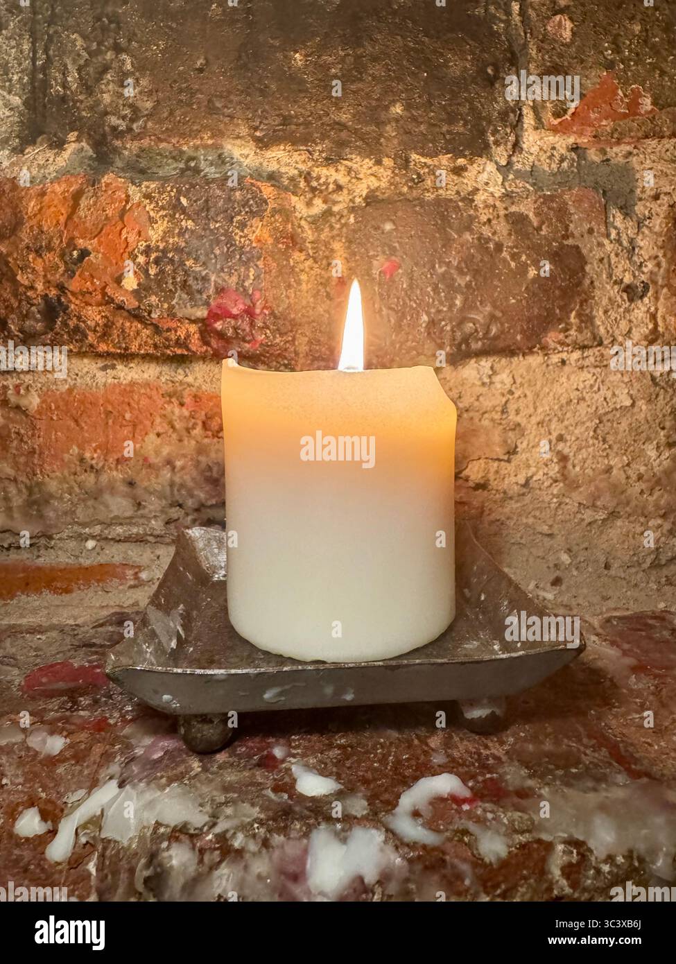 Lit white candle on a rustic metal holder against an old brick wall in Germany. - Smartphone Captured Stock Image