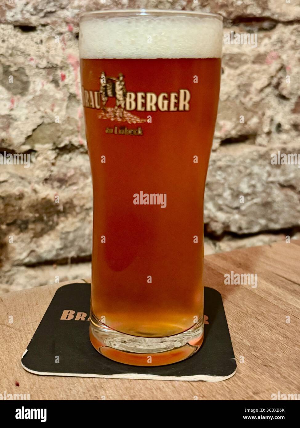 Glass of Brauberger beer on a coaster against a rustic stone wall in Lübeck, Germany. - Smartphone Captured Stock Image