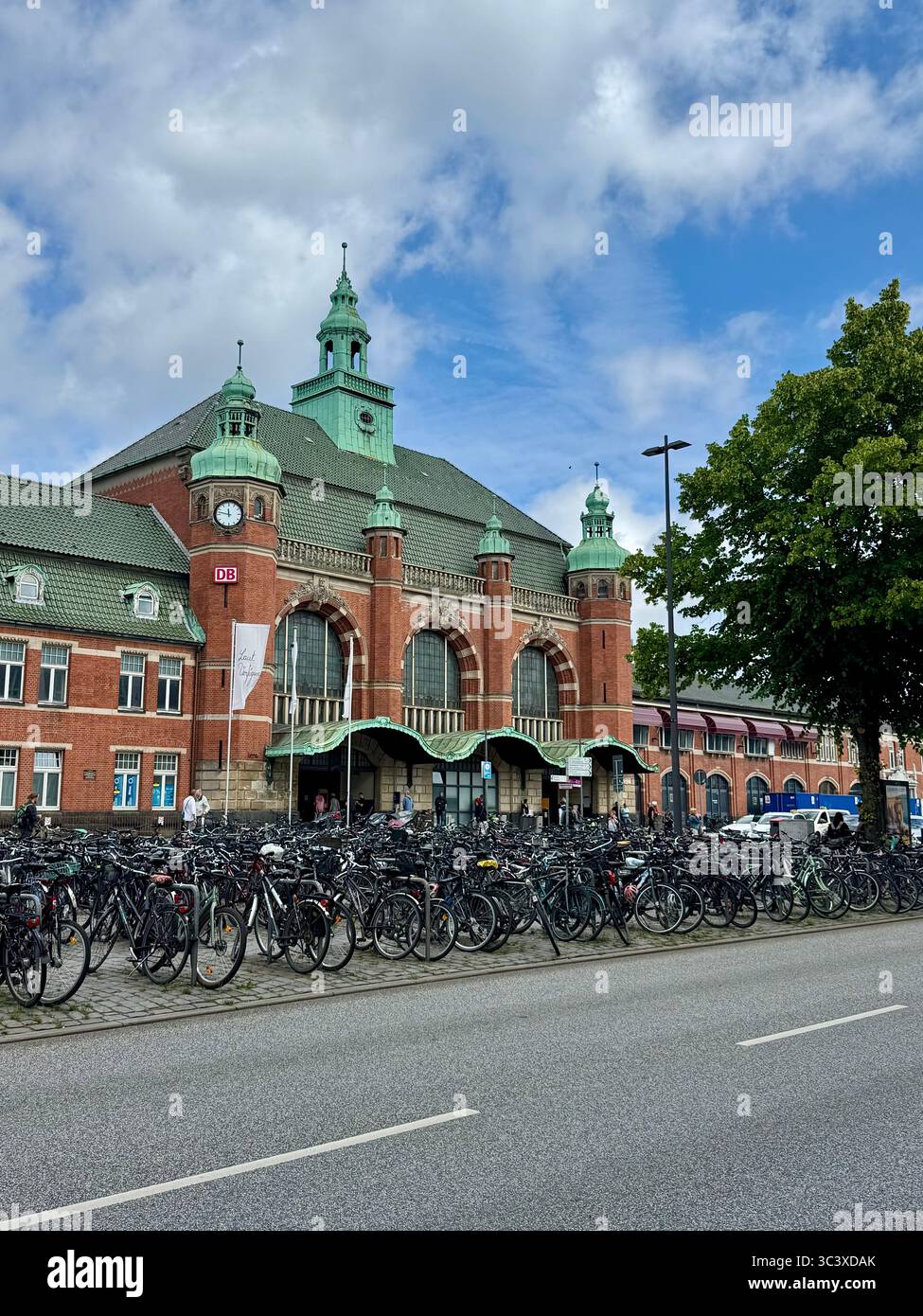 Lübeck Hauptbahnhof (main train station) with rows of parked bicycles in the foreground under a partly cloudy sky, Lübeck, Germany. - Smartphone Captured Stock Image