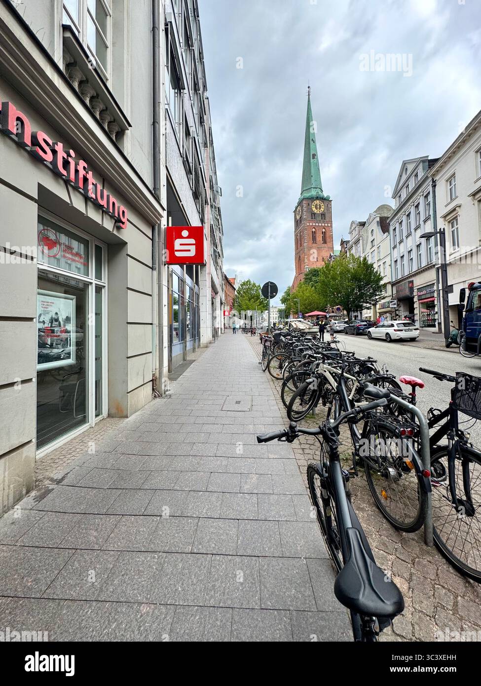 Bicycles parked along a street in Lübeck, Germany, with the spire of St. Mary's Church (Marienkirche) visible in the background on a cloudy day. - Smartphone Captured Stock Image Bicycles parked along a street in Lübeck, Germany, with the spire of St. Mary's Church (Marienkirche) visible in the background on a cloudy day. - Smartphone Captured Stock Image