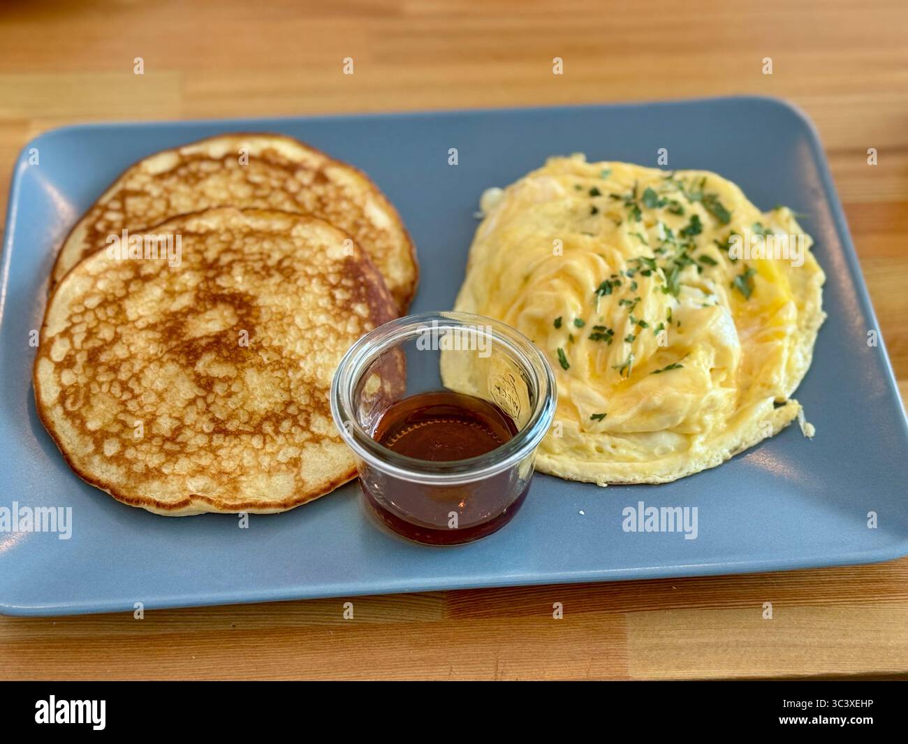 Plate of fluffy pancakes served with creamy scrambled eggs and a small glass container of syrup, Lübeck, Germany. - Smartphone Captured Stock Image