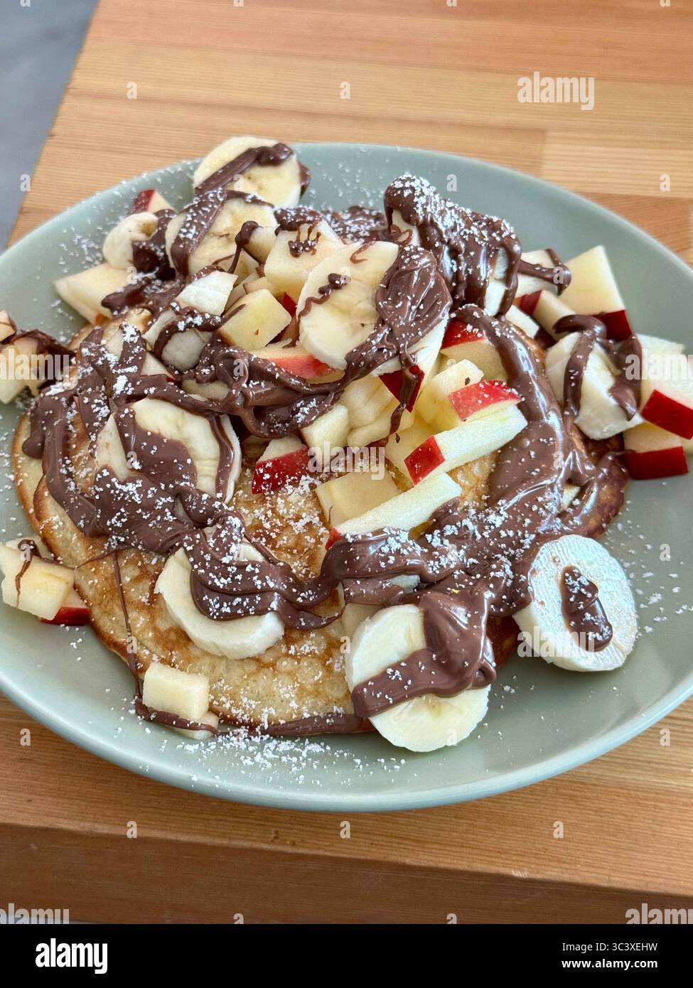 Delicious pancakes topped with banana slices, apple pieces, and drizzled with chocolate sauce, Lübeck, Germany. - Smartphone Captured Stock Image