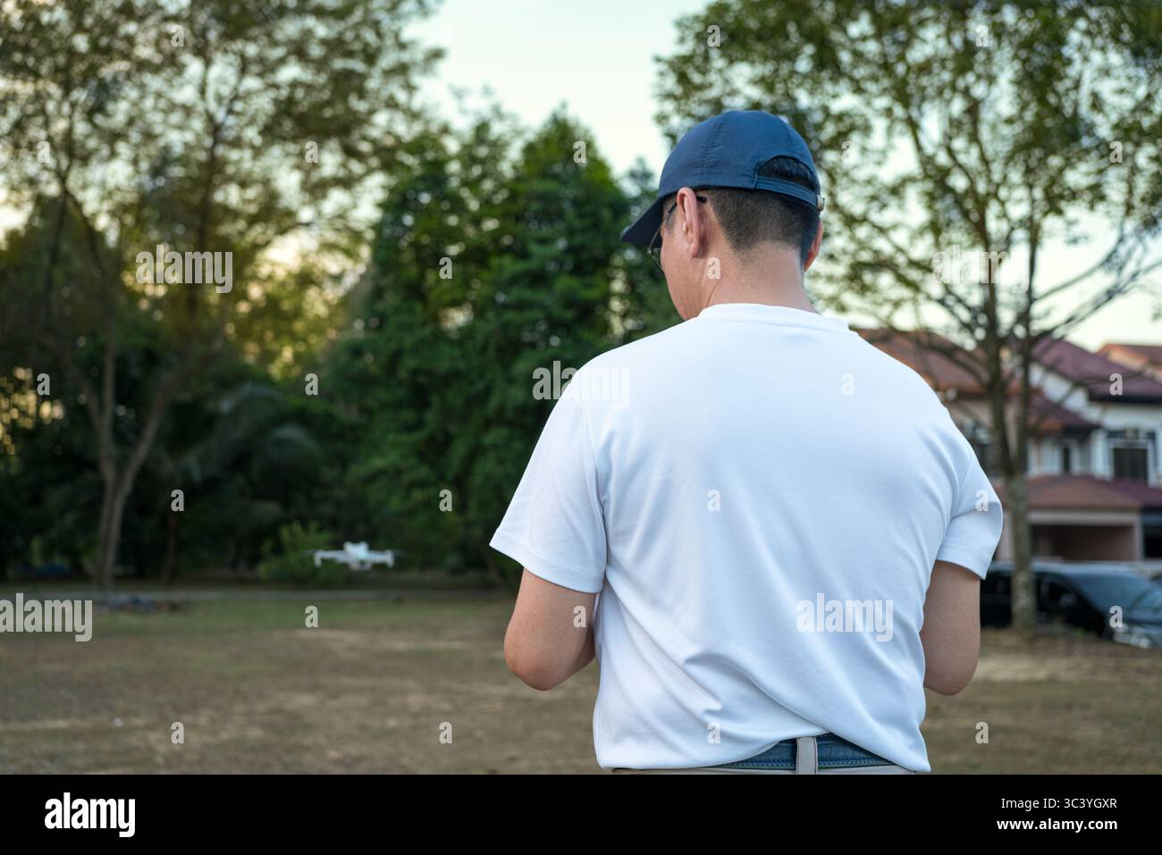 Man operating drone with controller standing with back on a field. Stock Photo