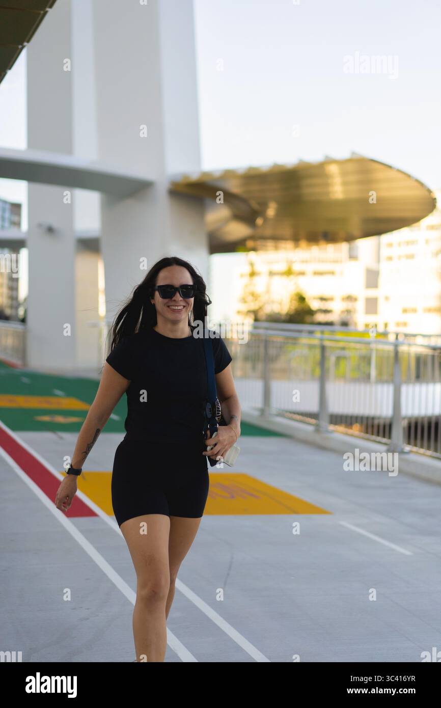 Woman walking outdoors in activewear with sunglasses on bright day Stock Photo