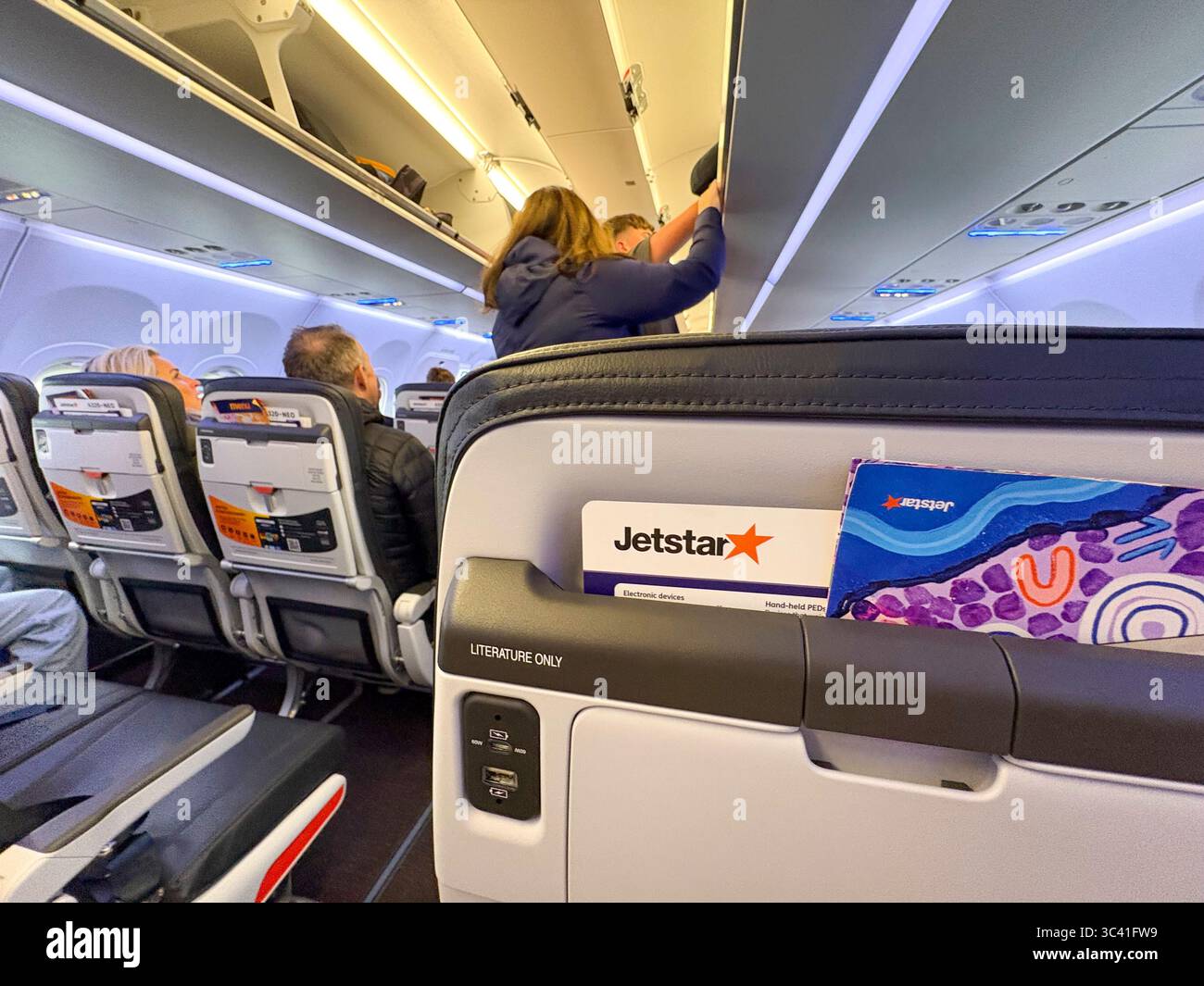 Jetstar aeroplane cabin of Airbus A320 NEO place cabin luggage in overhead locker on flight from Sydney Melbourne,Australia Stock Photo