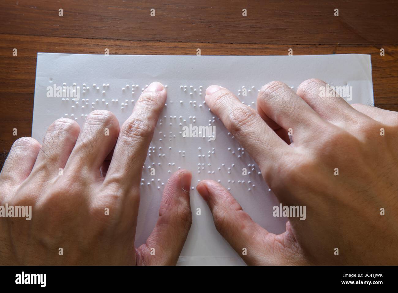 Visually impaired individuals use their fingertips to perceive Braille on paper, allowing them to read. Text on the paper is a dummy Lorem ipsum text. Stock Photo