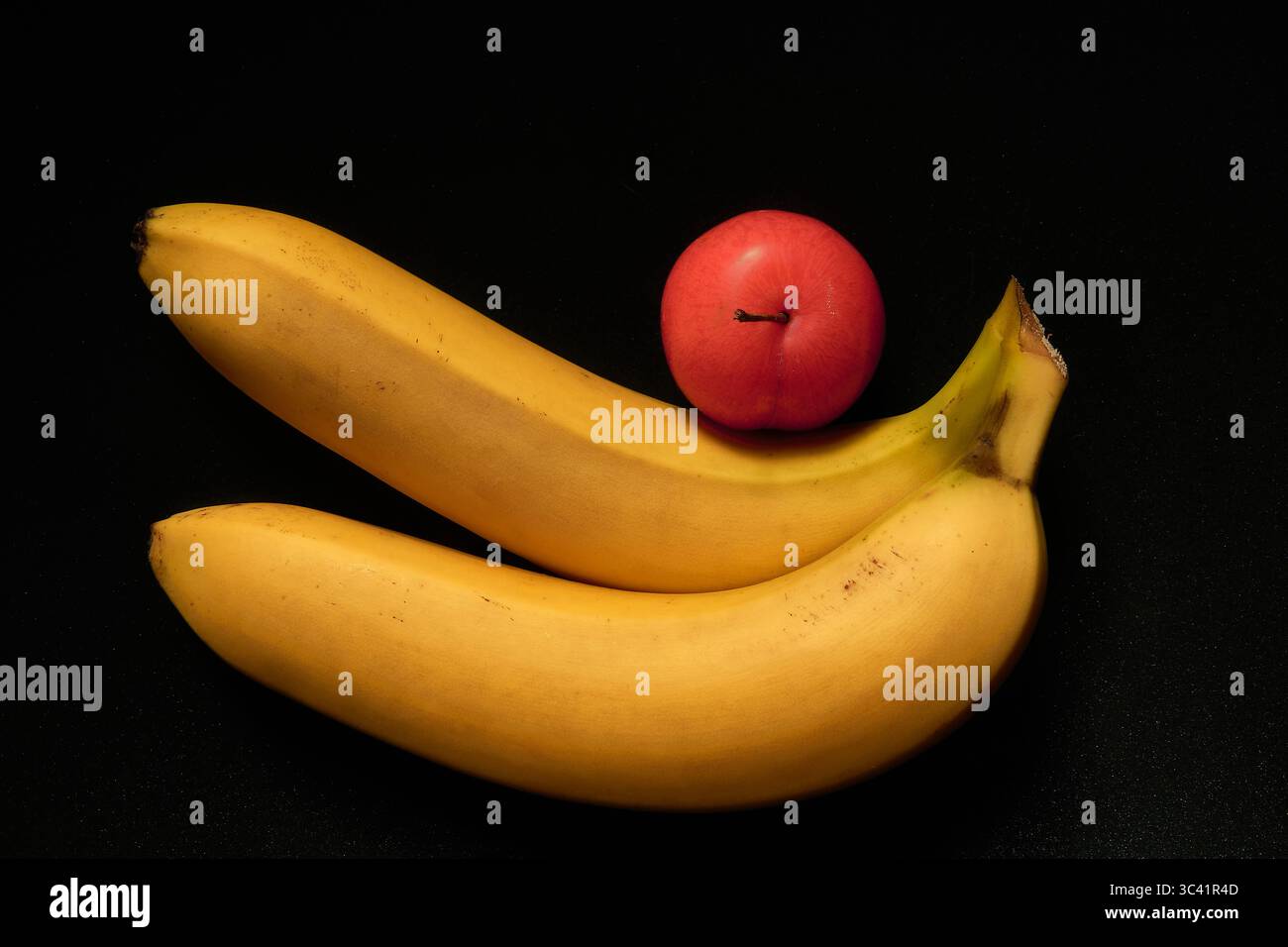 Still Life Photograph of Fresh Bananas and Red Plum Against a Contrasting Black Background Stock Photo