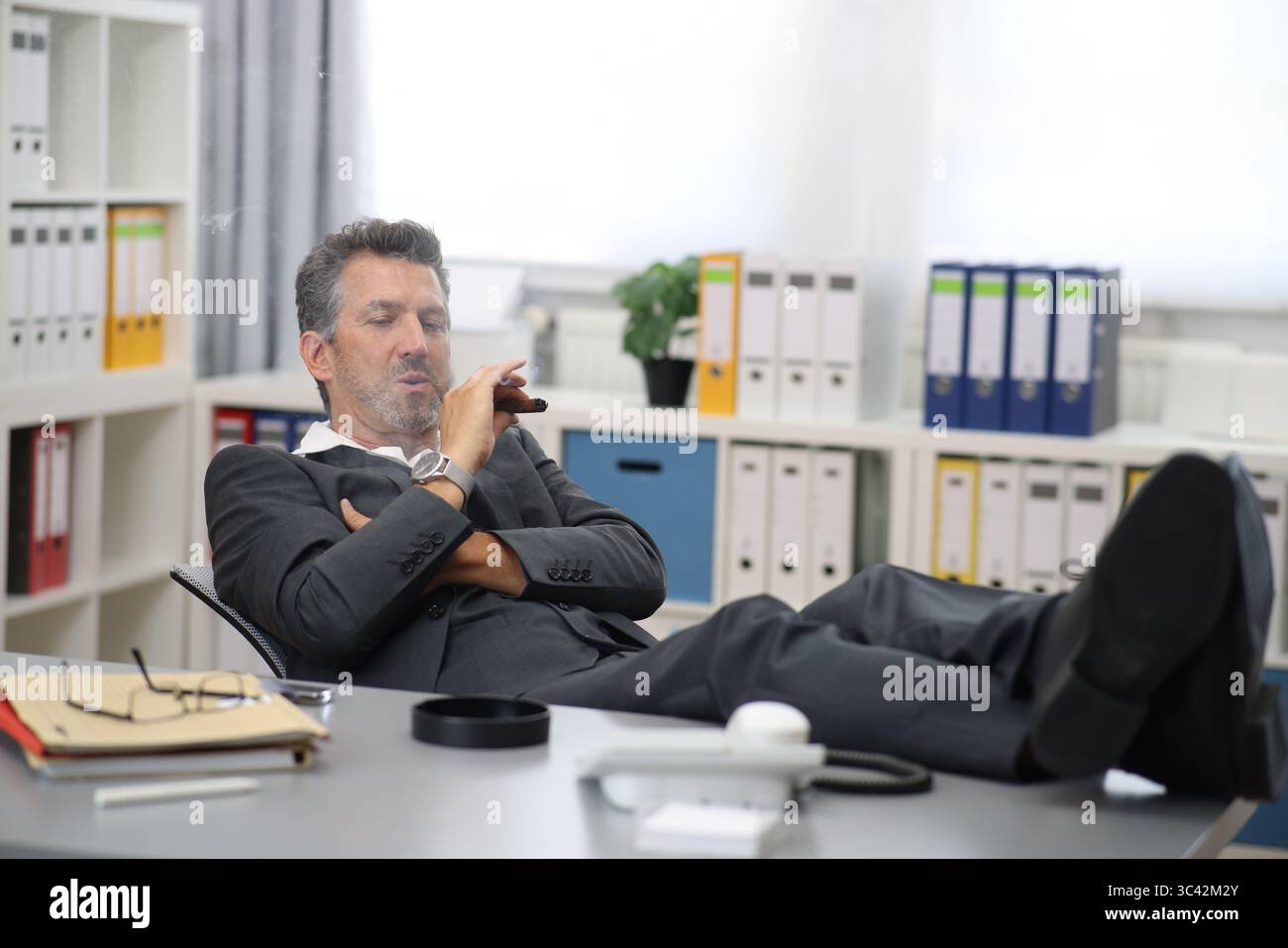 Man in office smoking with cigarette and feet on the table Stock Photo