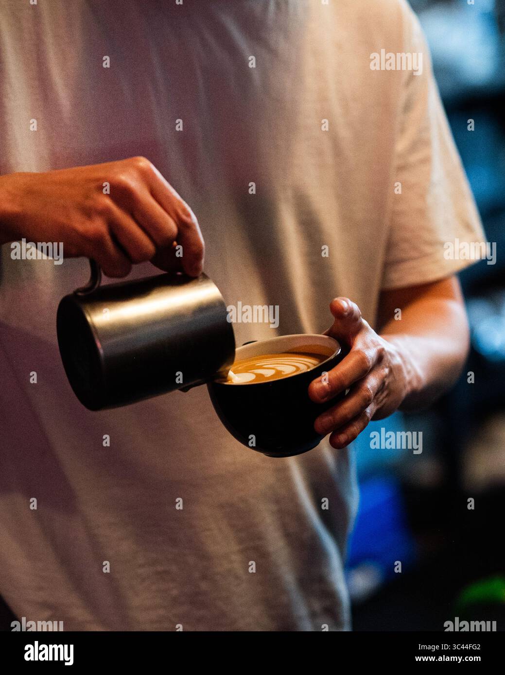 Close-up of a barista hands creating latte art in a coffee cup. Professional coffee preparation captured in a cozy cafe environment, highlighting the Stock Photo