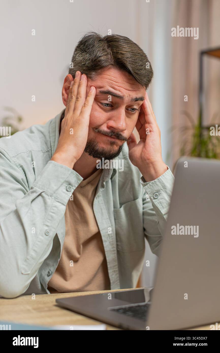 Angry furious man freelancer using laptop while working at home office having nervous breakdown at work, stress management, mental distress problems, losing temper, reaction on failure. Vertical. Stock Photo