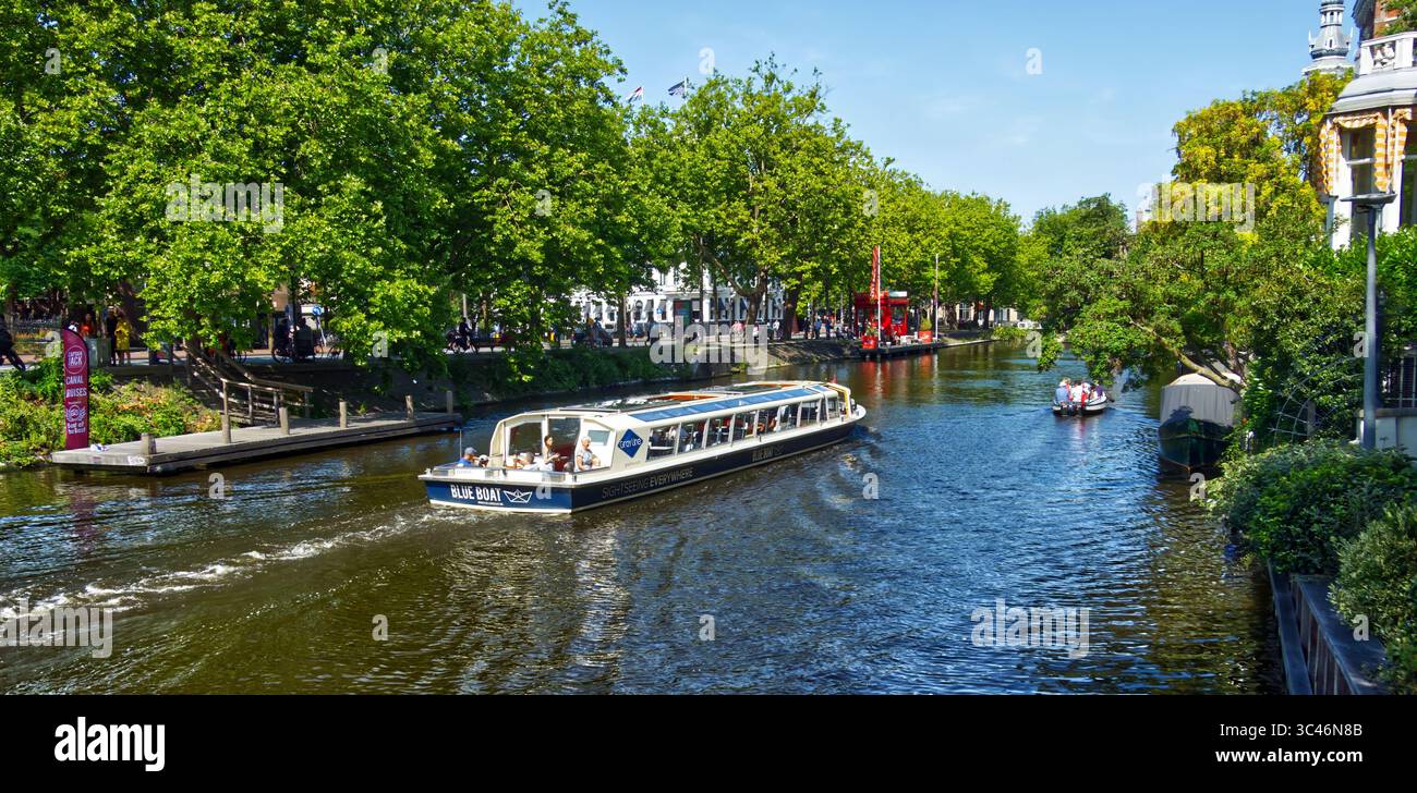 Amsterdam, netherlands, july 12,2025, tour boat navigating a picturesque amsterdam canal, carrying tourists on a summer sightseeing excursion, with lu Stock Photo