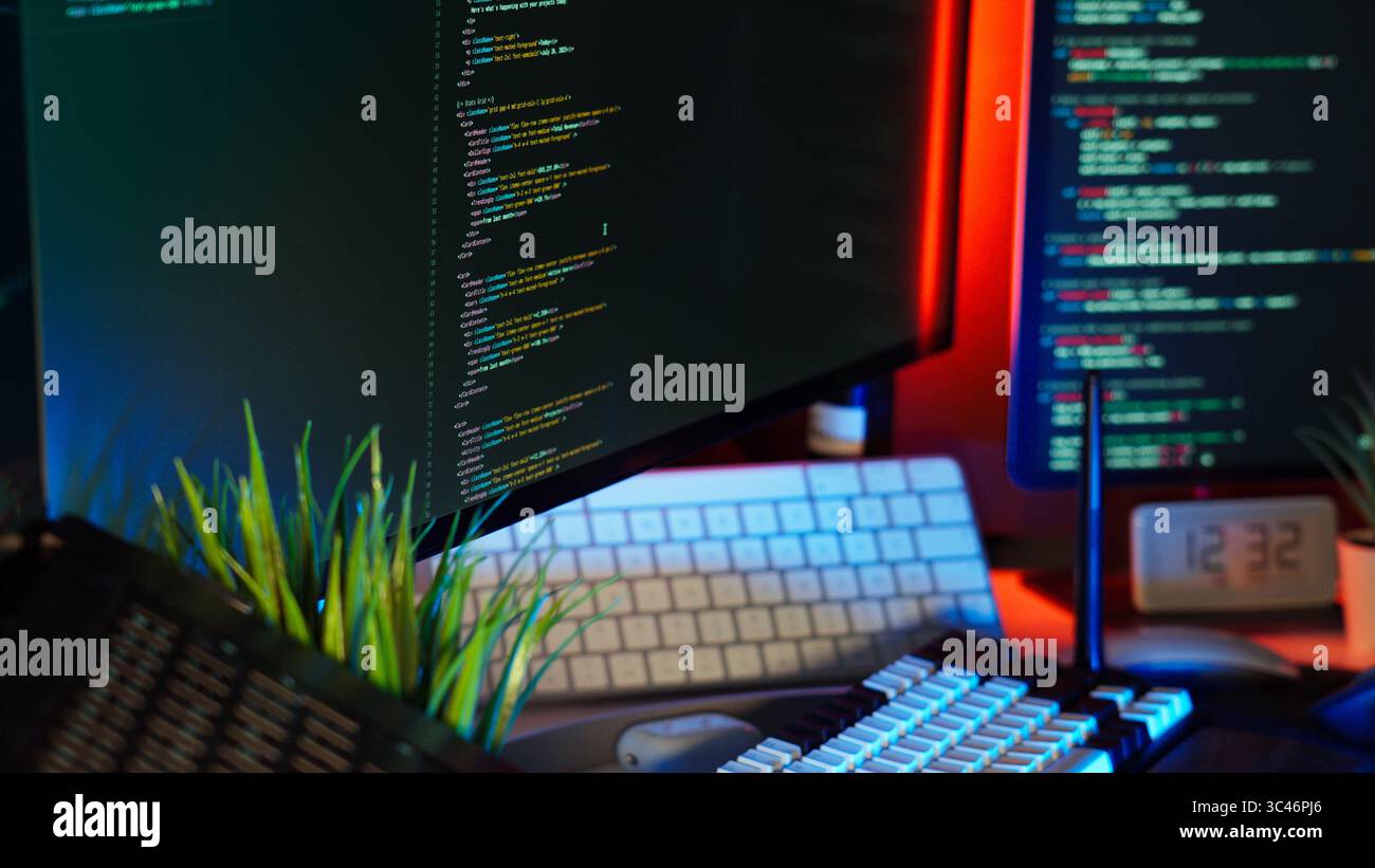 Code monitor home office color lighting setup featuring modern workspace with keyboard, plant decor and glowing screens. Abstract shot representing so Stock Photo