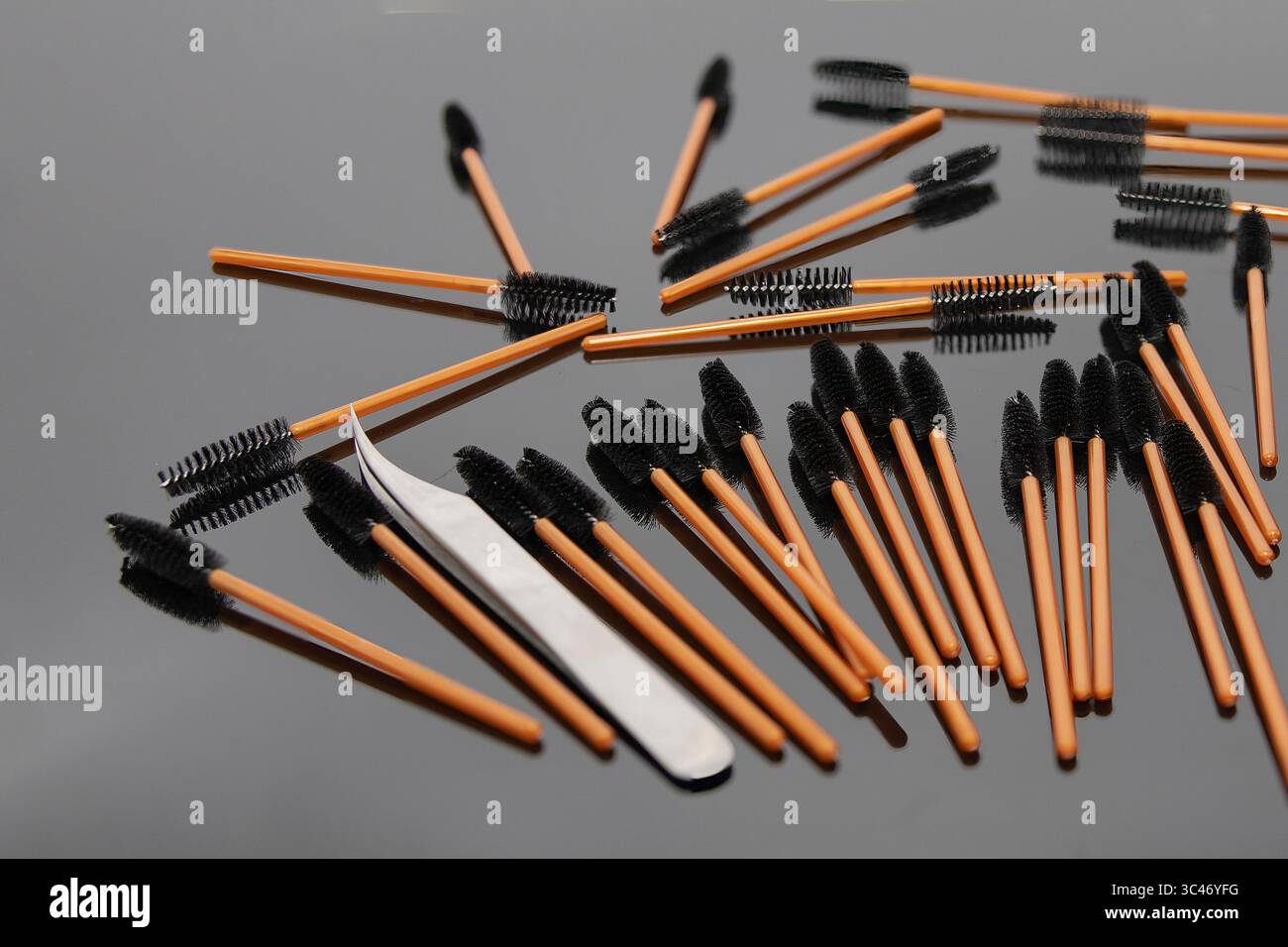 Scattered disposable eyelash brushes and metal tweezers on a glossy black background. Professional tools for lash extension, beauty salon, makeup, and Stock Photo