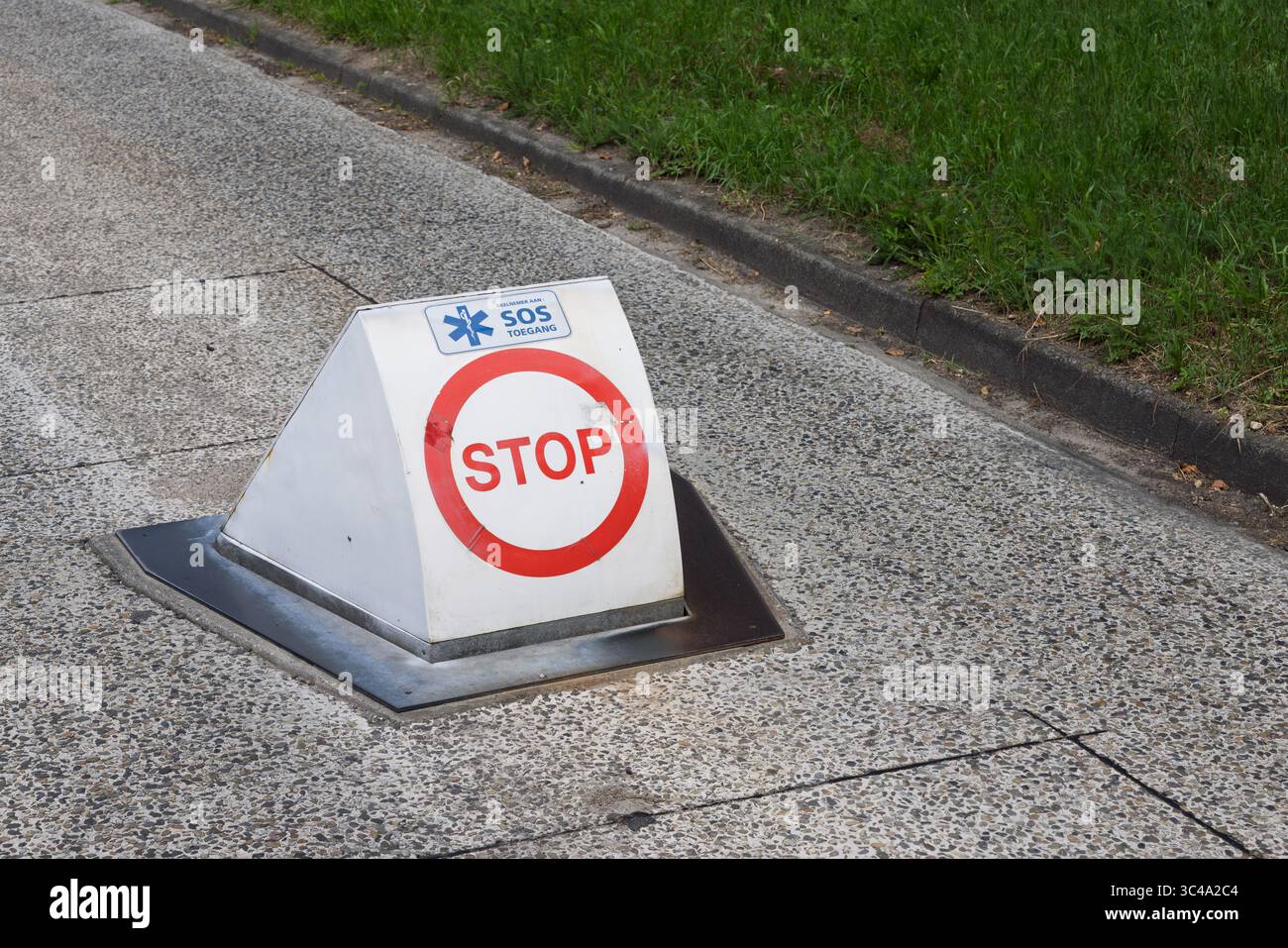 A "STOP" sign with an "SOS Toegang" (SOS Access) logo on a triangular white marker, set into the ground near a grassy area, indicating an emergency ac Stock Photo