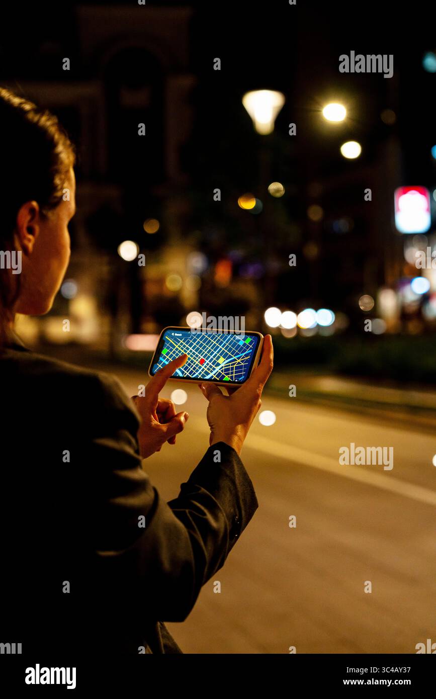 Female pedestrian using mobile navigation app on city street at night ...