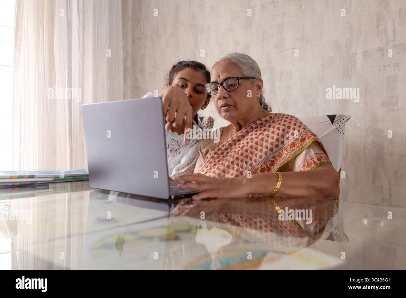 Indian Granddaughter Teaching Senior Woman (Grandmother) to Use Laptop at Home. Working Together on School Assignment using laptop. Stock Photo