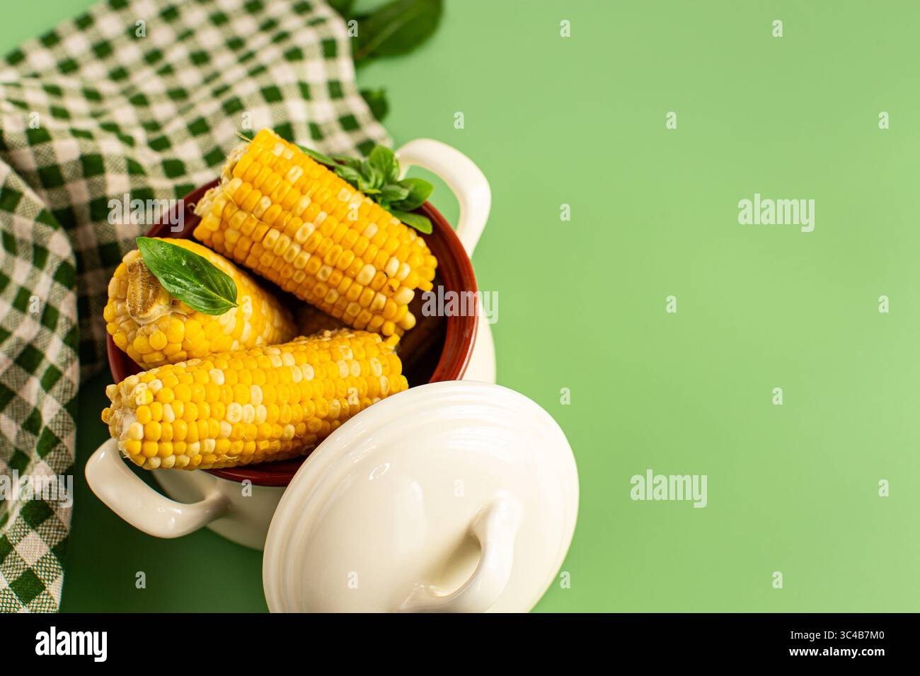 Hot corn cobs with greens on a green background. Stock Photo