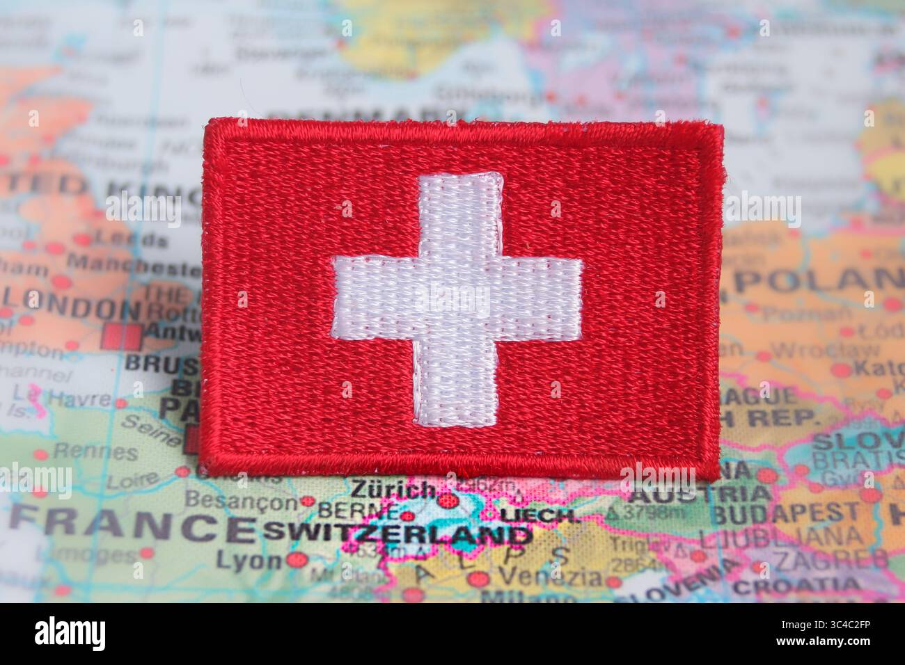Eco-friendly embroidered Swiss flag patch placed over Switzerland on a world map. Ideal for green travel, Europe tourism, and sustainability themes. Stock Photo