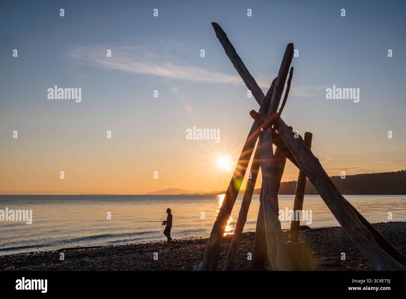 A person in silhouette fishing at sunset on the shore of a beach in British Columbia, Canada. Stock Photo