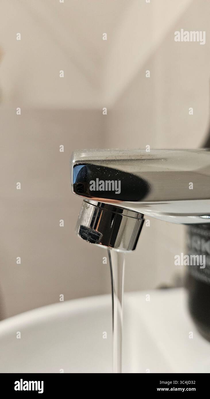A close-up photograph of a modern chrome faucet pouring a clear stream of water into a pristine white sink bowl. - Smartphone Captured Stock Image