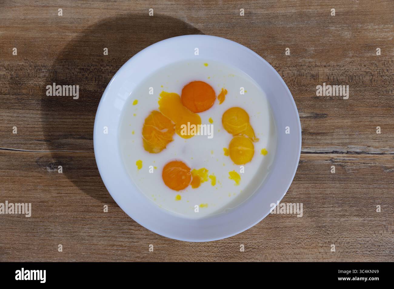 A Delicious Display of Fresh Egg Yolks and Cream Blended Together in a White Bowl Arranged on a Rustic Wooden Table for a Culinary Presentation Stock Photo