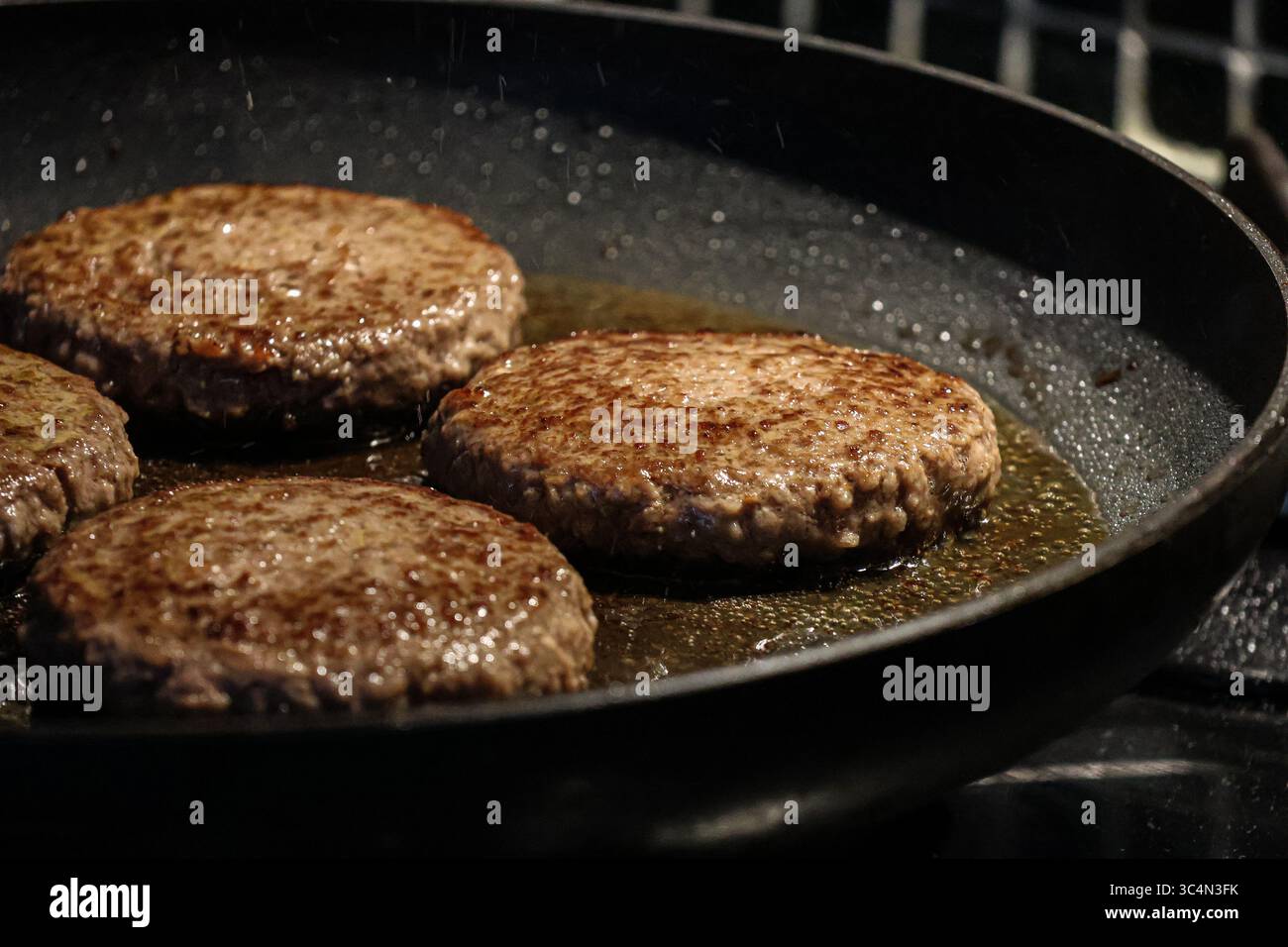 Sizzling perfection! Juicy burgers browning in a hot pan, ready to tempt any taste buds. Stock Photo