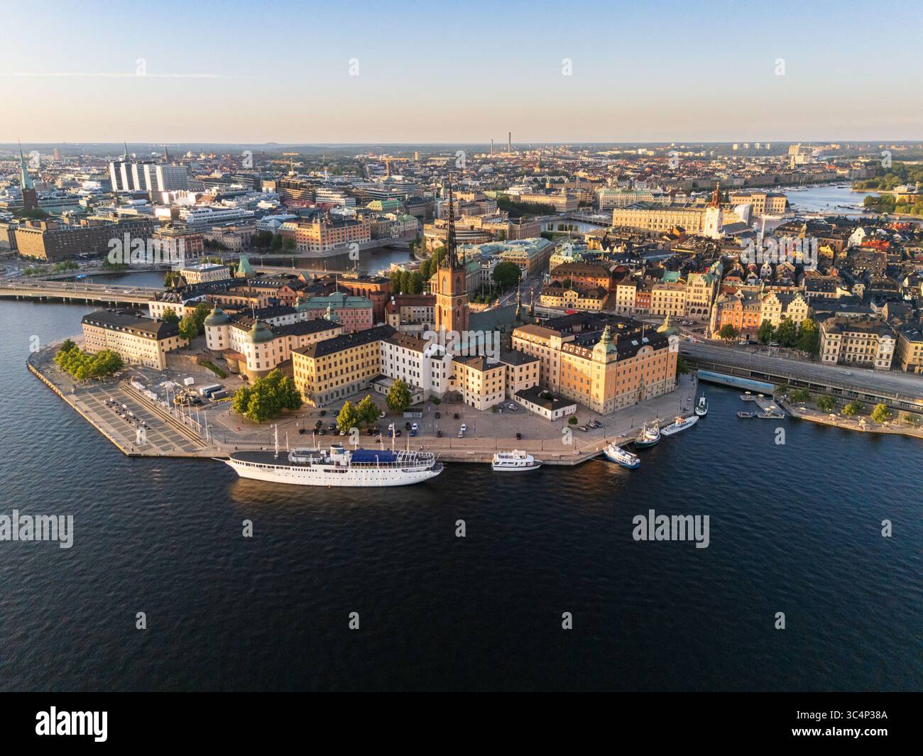 Aerial view of the sun-kissed Riddarholmen island with its historic church and boats contrasting the deep blue waters of Lake Mälaren, Stockholm, Swed Stock Photo