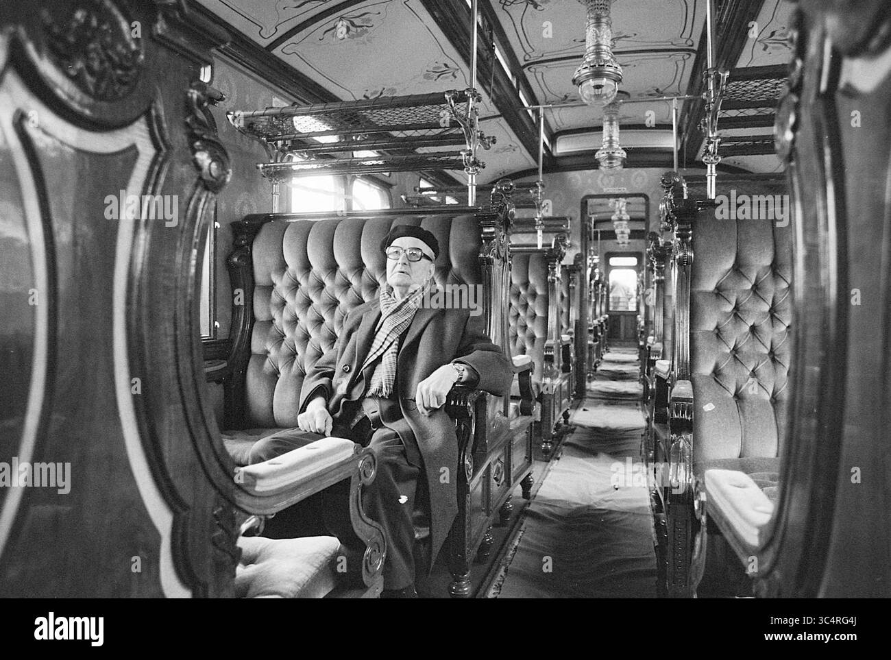 Restored railway carriage + hr. Karskens, Treinen, 12-04-1977 Whizgle News, Dutch Desk, The Netherlands, 1950-2000 An elderly man sits elegantly in a vintage train carriage, surrounded by plush, tufted seating and ornate wooden details, evoking a sense of nostalgia for a bygone era of luxury travel. Stock Photo