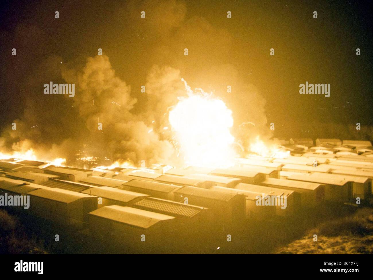 Fire at beach houses, IJmuiden, IJmuiden, The Netherlands, 03-01-2004 Whizgle News, Dutch Desk, The Netherlands, 1950-2000 An intense explosion lights up the night sky, sending flames and smoke billowing above a row of structures below. The scene captures a chaotic moment, with bright light contrasting against a backdrop of darkness. Stock Photo