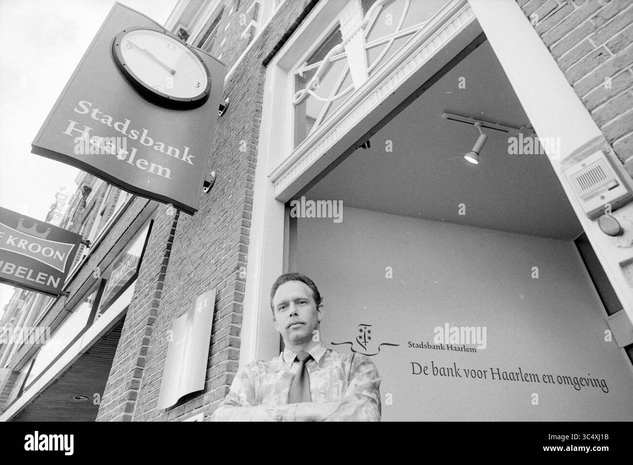 Jos Stevens, Stadsbank, Haarlem, The Netherlands, 13-04-1994 Whizgle News, Dutch Desk, The Netherlands, 1950-2000 A man stands confidently outside the Stadsbank Haarlem, with a large clock above him marking the time. The bank's sign features its name prominently, while details of its services are visible on the entrance wall. Stock Photo