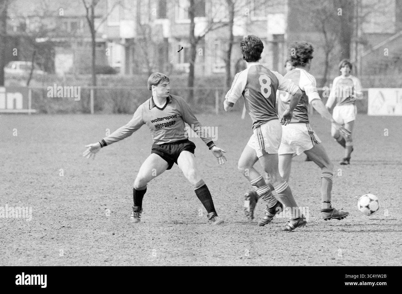 Zandvoort Meeuwen - DWS, Football Zandvoortse Meeuwen Halfweg, 10-04-1983 Whizgle News, Dutch Desk, The Netherlands, 1950-2000 A goalkeeper, wearing a black kit, stands ready in the penalty area, arms outstretched, as two opposing players in matching orange and yellow uniforms maneuver the ball nearby on a muddy field. The intensity of the match is palpable, with a backdrop of a quiet residential area. Stock Photo