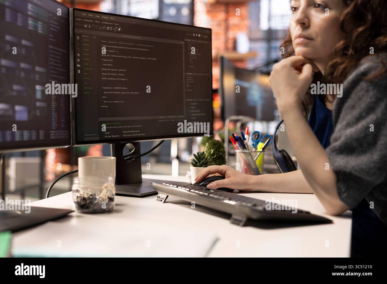 Female programmer seen typing code for a user interface design on dual monitors, working in a digital workspace. Woman IT specialist working on software engineering and front end development. Stock Photo